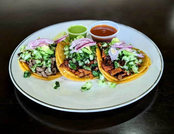 three tacos with meat, lettuce, and sauce on a white plate